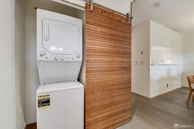 clothes washing area featuring a barn door, laundry area, wood finished floors, baseboards, and stacked washer / drying machine