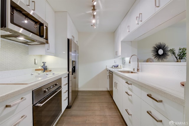 kitchen with backsplash, light wood-style flooring, appliances with stainless steel finishes, white cabinets, and a sink