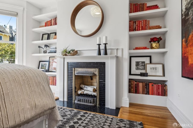 interior space with a tiled fireplace, built in shelves, and wood finished floors