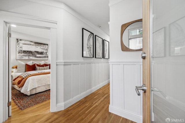 corridor with wood finished floors, wainscoting, and a decorative wall
