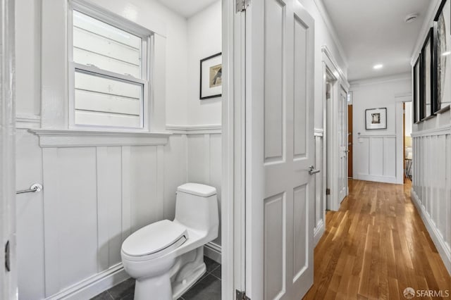 bathroom featuring a decorative wall, toilet, wainscoting, and wood finished floors