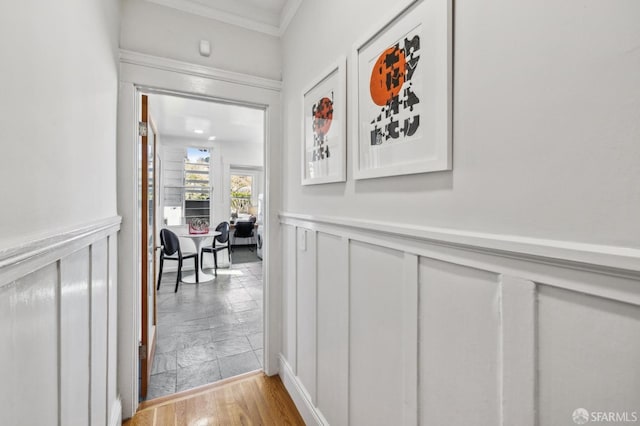 corridor with ornamental molding and a wainscoted wall