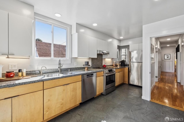 kitchen featuring dark stone countertops, recessed lighting, under cabinet range hood, stainless steel appliances, and a sink