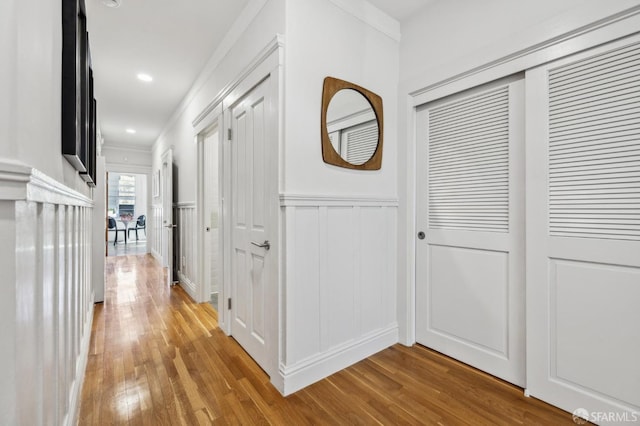 corridor featuring a decorative wall, crown molding, a wainscoted wall, and wood finished floors
