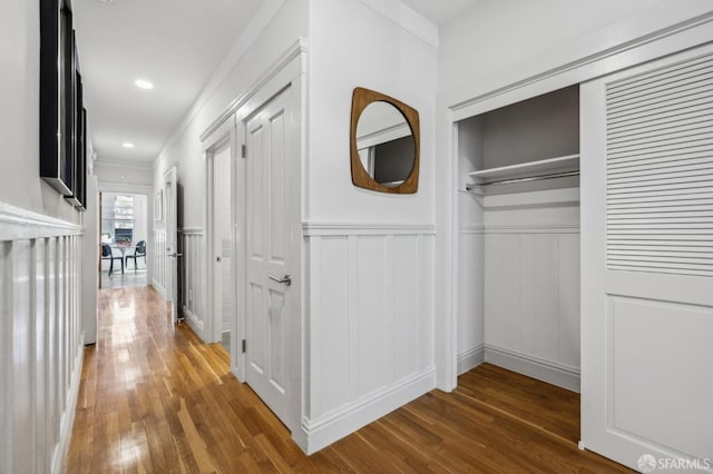 hallway with crown molding, a decorative wall, wainscoting, and wood finished floors