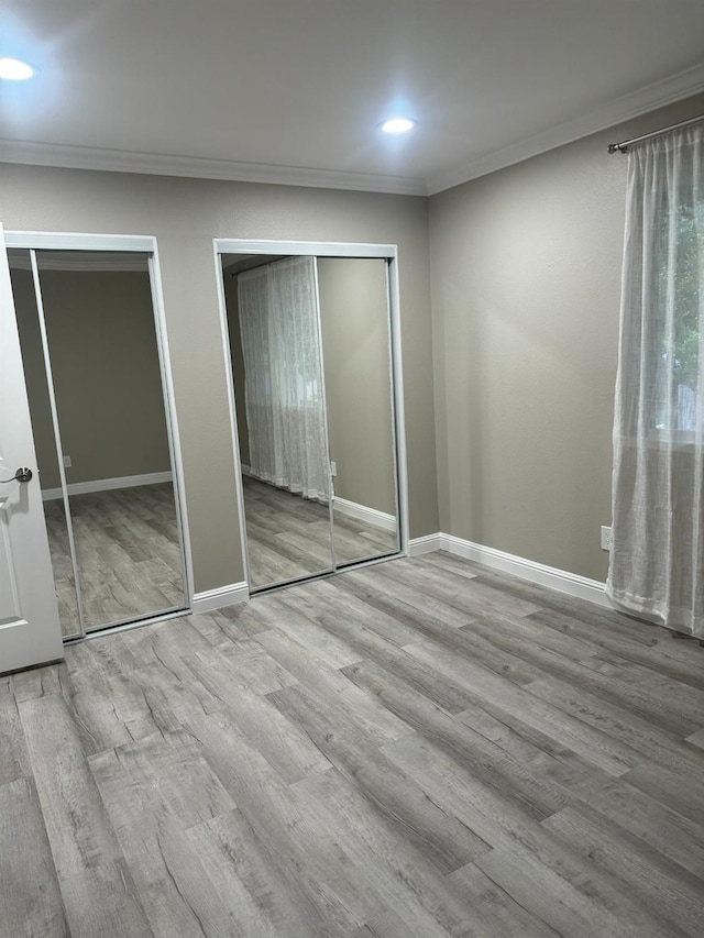 unfurnished bedroom with multiple closets, ornamental molding, and light wood-type flooring