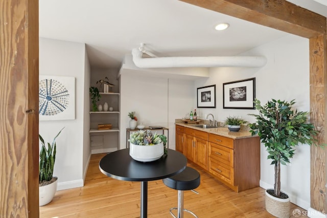 bar featuring light stone countertops, light hardwood / wood-style floors, and sink