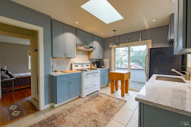 kitchen with white range with gas cooktop, a sink, under cabinet range hood, freestanding refrigerator, and a skylight