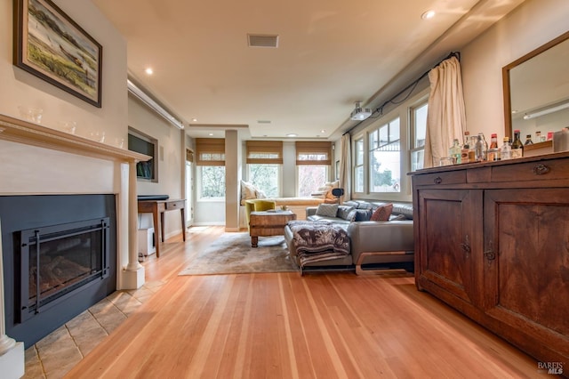 living room featuring recessed lighting, a fireplace with flush hearth, a healthy amount of sunlight, and light wood-style flooring