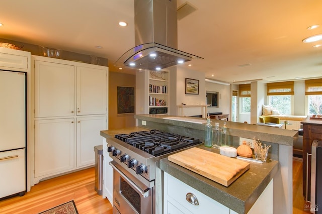 kitchen with high end stainless steel range oven, open floor plan, white cabinetry, freestanding refrigerator, and island range hood