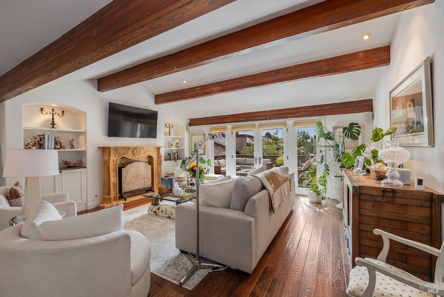 living area with built in shelves, a premium fireplace, dark wood-style flooring, and beamed ceiling