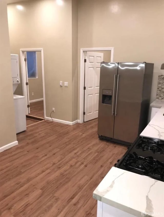 kitchen with stacked washer and dryer, light stone counters, stainless steel fridge, light wood finished floors, and baseboards