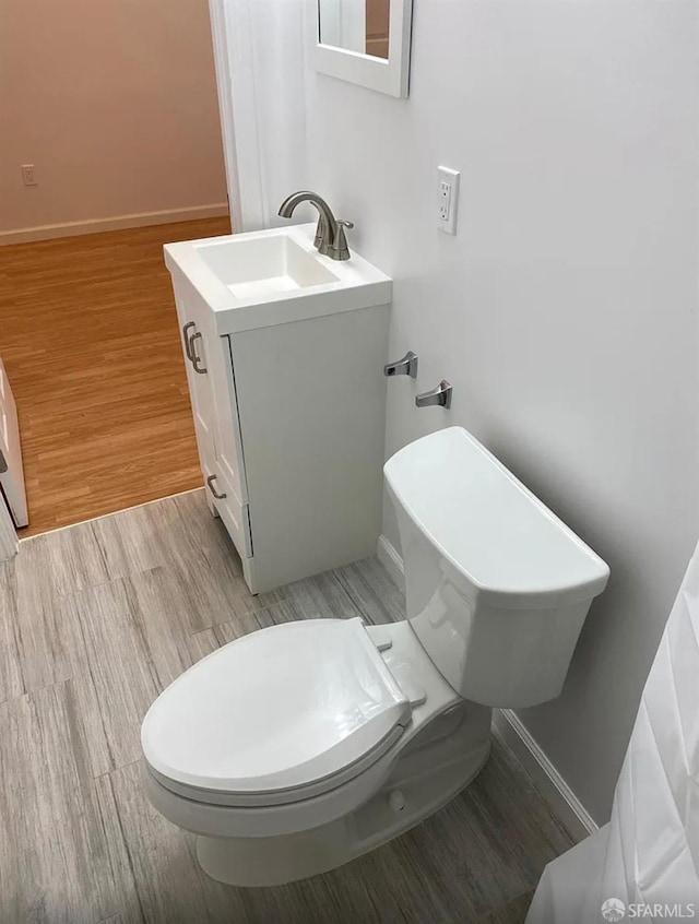 bathroom featuring baseboards, toilet, wood finished floors, and vanity