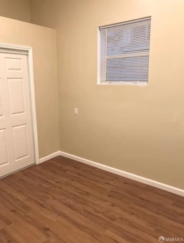 unfurnished room with baseboards and dark wood-style flooring