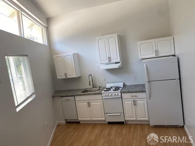 kitchen with white appliances, light wood finished floors, a high ceiling, a sink, and white cabinets