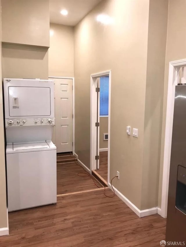 laundry area with baseboards, laundry area, a towering ceiling, wood finished floors, and stacked washer / drying machine