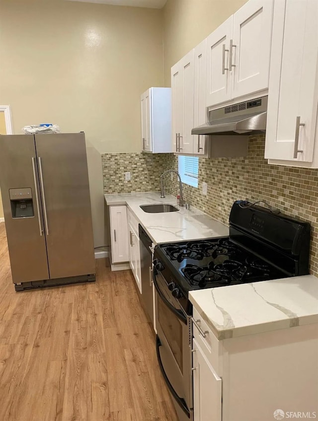 kitchen with a sink, under cabinet range hood, appliances with stainless steel finishes, white cabinetry, and light wood-type flooring