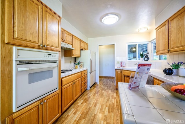 kitchen with sink, white appliances, tasteful backsplash, tile countertops, and light wood-type flooring