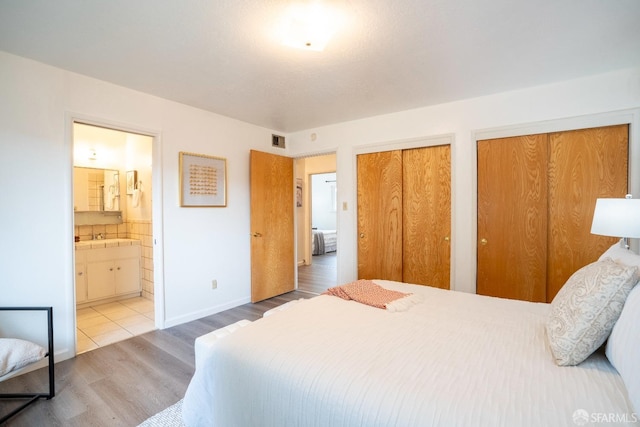 bedroom with connected bathroom, hardwood / wood-style floors, and two closets