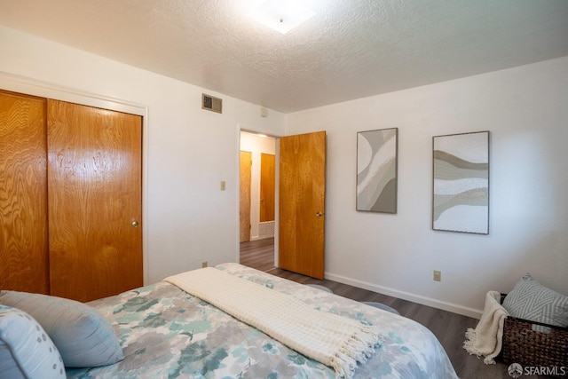 bedroom with dark wood-type flooring, a textured ceiling, and a closet