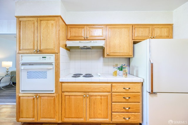 kitchen featuring tasteful backsplash, white appliances, tile counters, and light wood-type flooring