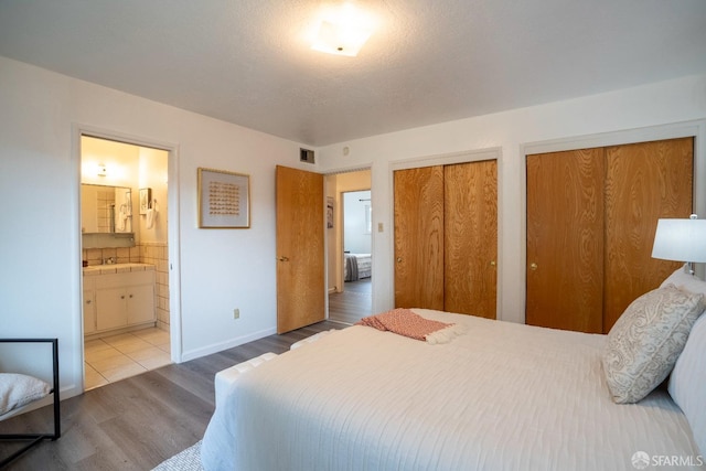 bedroom featuring hardwood / wood-style flooring, connected bathroom, and two closets