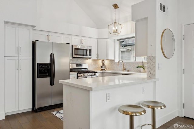 kitchen featuring stainless steel appliances, vaulted ceiling, hanging light fixtures, and white cabinets