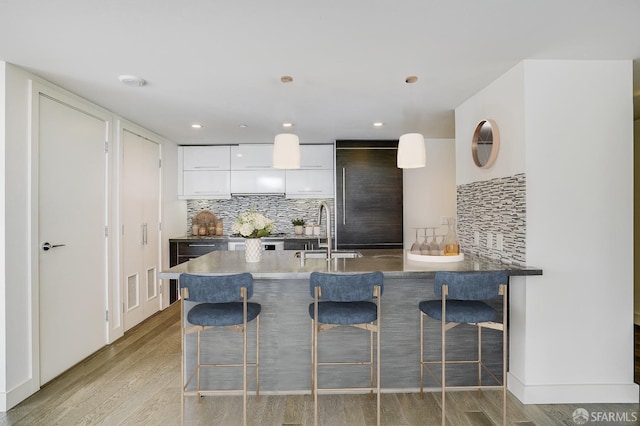 kitchen featuring backsplash, light wood-type flooring, sink, pendant lighting, and white cabinets