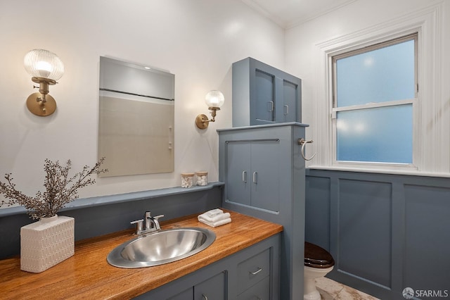 bathroom with toilet, ornamental molding, a decorative wall, and vanity