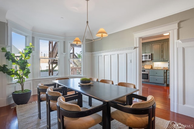 dining room with dark wood-style floors, wainscoting, and a decorative wall