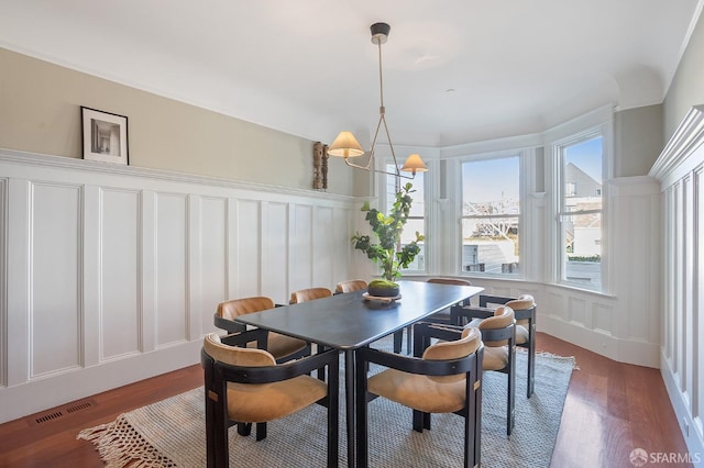 dining area featuring a chandelier, dark wood-style flooring, visible vents, and a decorative wall