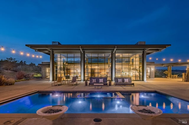 pool at night featuring an in ground hot tub, a patio area, and an outdoor living space