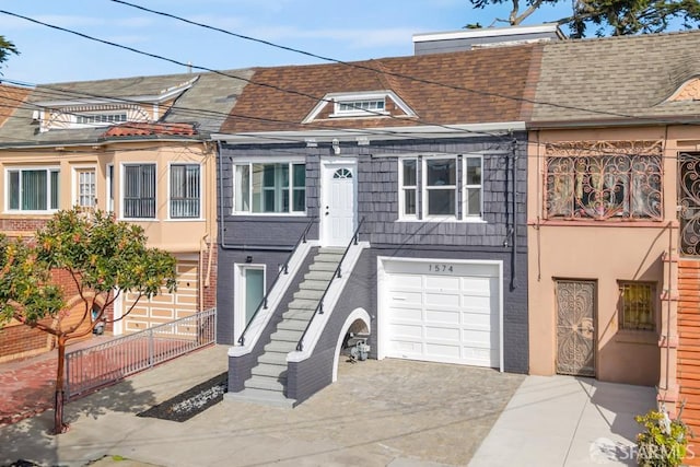 multi unit property featuring driveway, a shingled roof, a garage, brick siding, and stairs