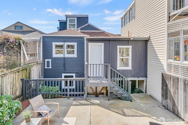 rear view of property featuring fence, roof with shingles, and a patio area