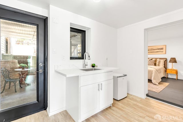 bar with refrigerator, baseboards, light wood-style floors, and a sink