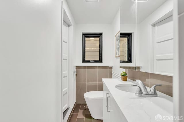 bathroom with a wainscoted wall, toilet, tile walls, and vanity