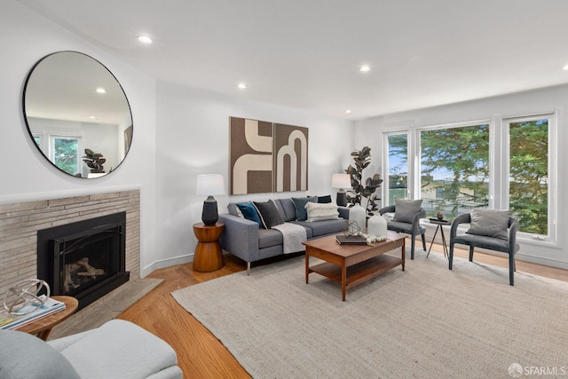 living room with light hardwood / wood-style flooring, a stone fireplace, and a wealth of natural light