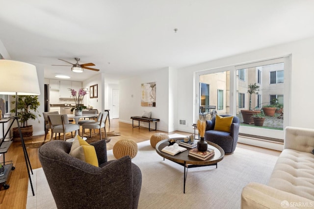 living area featuring a baseboard heating unit, ceiling fan, light wood-style flooring, and baseboards