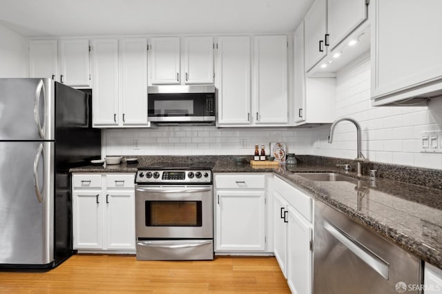 kitchen with decorative backsplash, dark stone counters, appliances with stainless steel finishes, light wood-style floors, and a sink