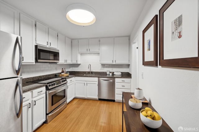 kitchen featuring stainless steel appliances, light wood-style floors, a sink, and decorative backsplash