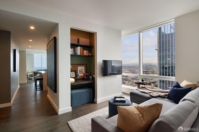 living area with built in shelves, dark wood-style flooring, a wall of windows, and baseboards