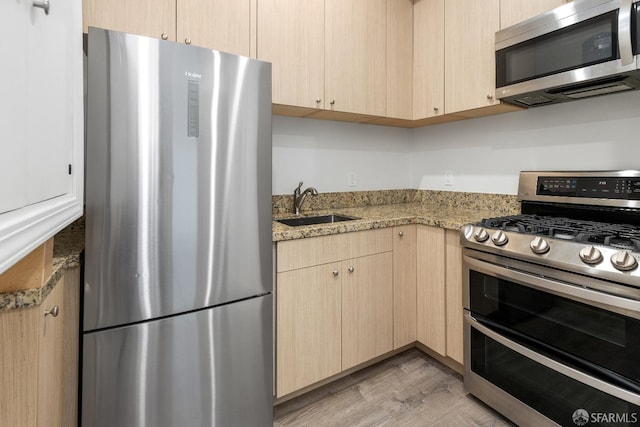 kitchen with sink, appliances with stainless steel finishes, light hardwood / wood-style floors, light stone countertops, and light brown cabinets