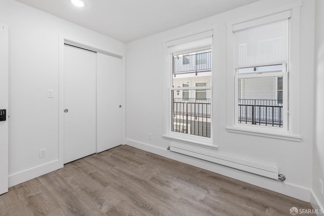 unfurnished bedroom featuring a baseboard radiator, light wood-type flooring, and a closet