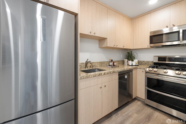 kitchen with appliances with stainless steel finishes, light brown cabinetry, sink, light stone counters, and light wood-type flooring