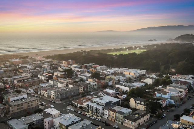 aerial view at dusk featuring a water view and a view of the beach