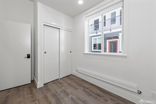 unfurnished bedroom with wood-type flooring, baseboard heating, and a closet