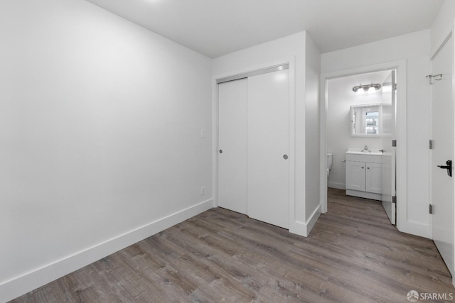 unfurnished bedroom with connected bathroom, sink, a closet, and light hardwood / wood-style flooring