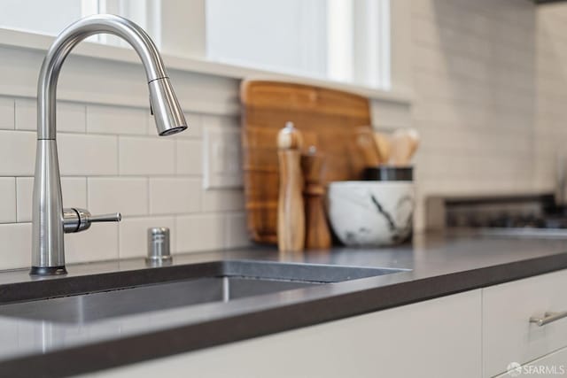 interior details featuring tasteful backsplash, white cabinetry, and sink