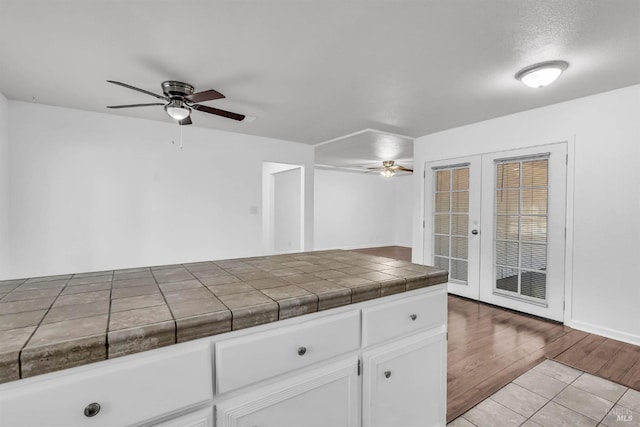 1607 California Dr, Vacaville, CA 95687 - kitchen featuring a ceiling fan, french doors, white cabinets, light wood-style flooring, and tile countertops