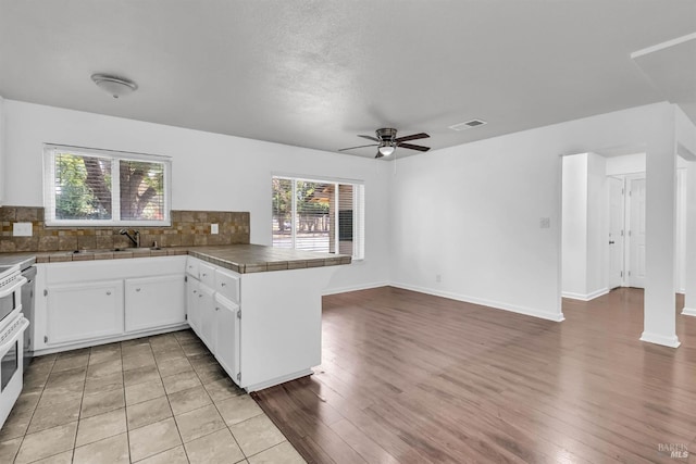 1607 California Dr, Vacaville, CA 95687 - kitchen with a peninsula, ceiling fan, tasteful backsplash, white cabinets, and light wood-style floors